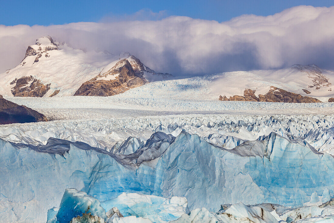 Formen und Strukturen von blau schimmerndem Eis am Perito Moreno Gletscher mit den Bergen im südlichen Eisfeld, Argentinien, Patagonien, Südamerika