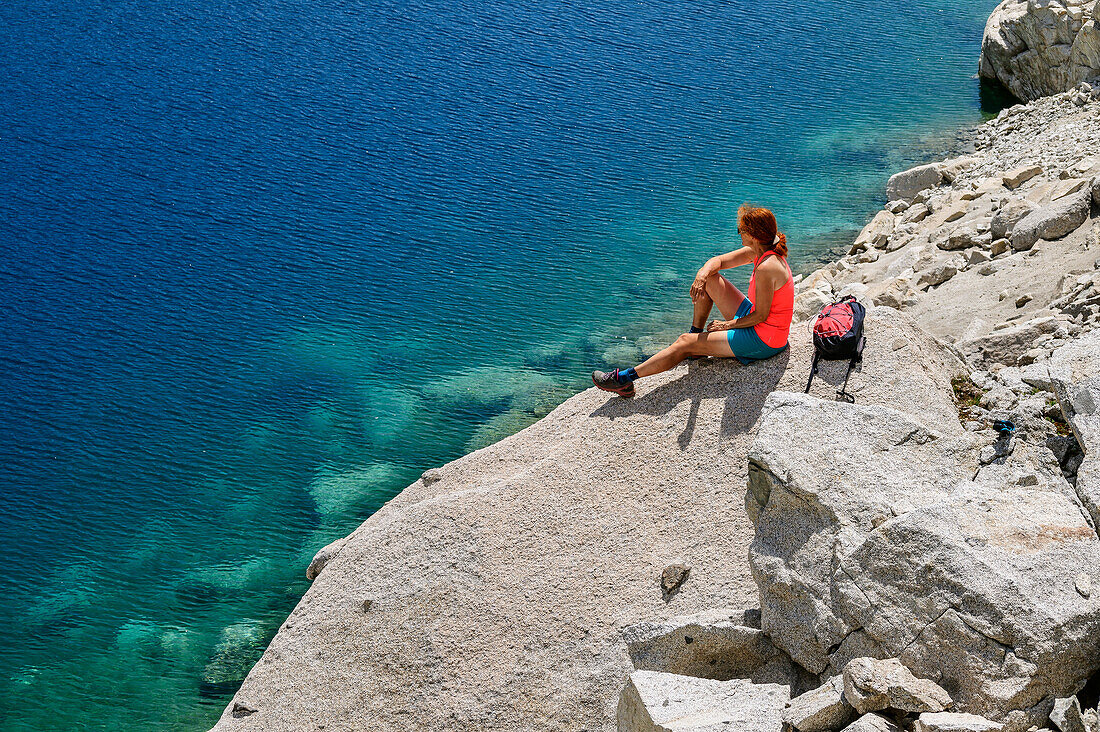 Frau beim Wandern sitzt auf Felsplatte über Bergsee, Estany de Mar, Nationalpark Aigüestortes i Estany de Sant Maurici, Katalonien, Pyrenäen, Spanien