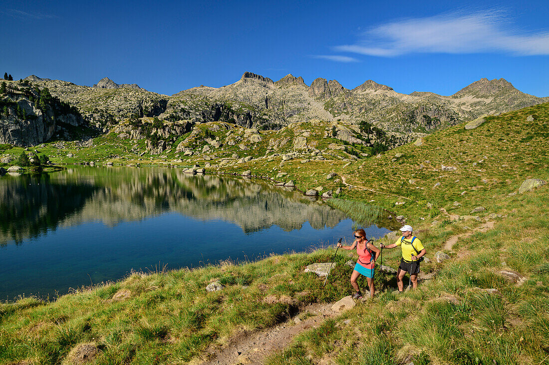 Mann und Frau beim Wandern gehen am Bergsee Estanh Plan vorüber, Circ de Colomers, Nationalpark Aigüestortes i Estany de Sant Maurici, Katalonien, Pyrenäen, Spanien