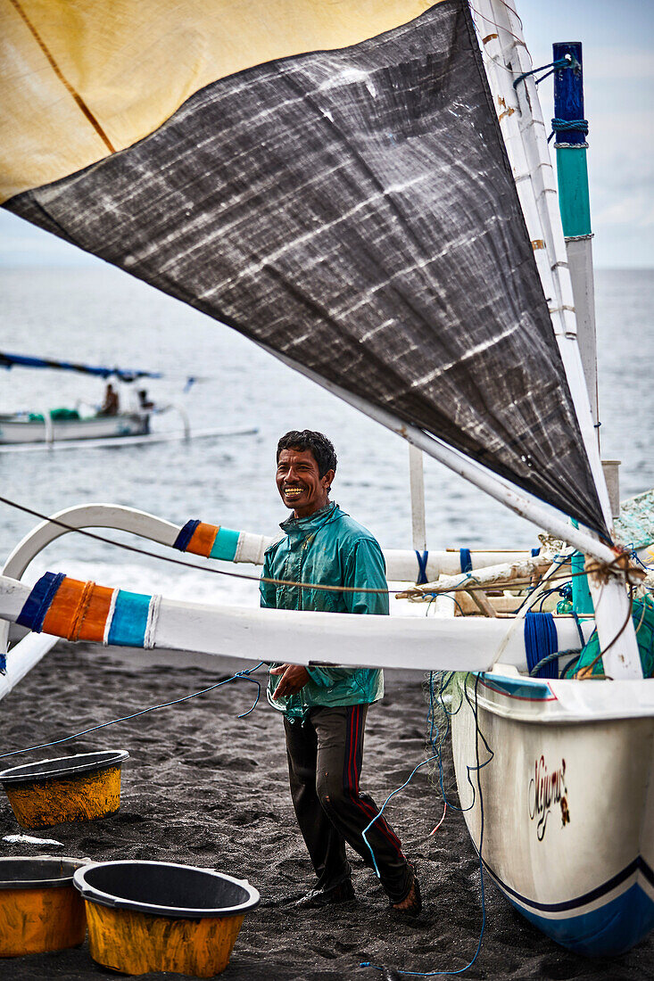 Ein lächelnder Fischer mit seinem Boot am Ende des Tages am Strand von Seraya, Karangasem Bali Indonesien