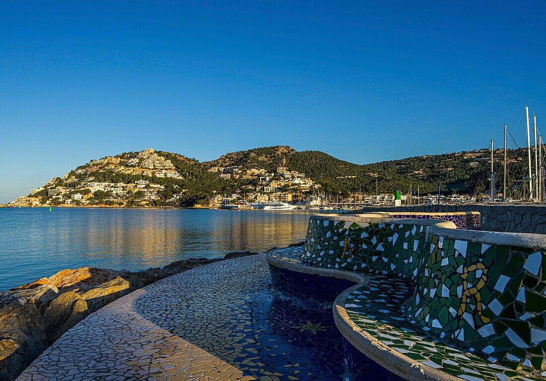 View from a stone bench on the shore of Port d'Andratx and the marina reflected in the sea, Mallorca, Spain