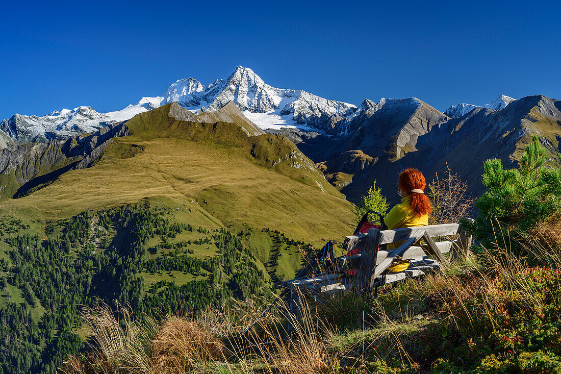 Woman hiking sitting on bench and looking at Grossglockner, Schönleitenspitze, Hohe Tauern, Hohe Tauern National Park, East Tyrol, Austria