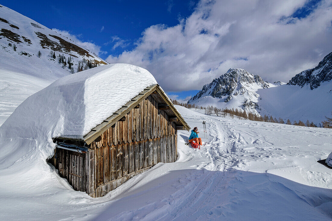 Woman on a ski tour sitting on a snow-covered alp with Bielschitza in the background, Matschacher Alm, Rosental, Karawanken, Carinthia, Austria