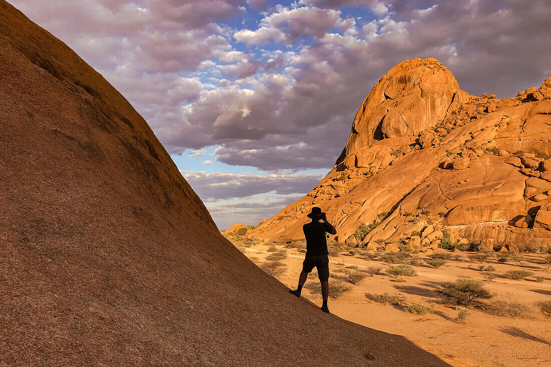 Silhouette von einem Fotograf, der ein Bild von den Felsen am Spitzkoppe Massiv macht bei Sonnenuntergang, Namibia, Afrika
