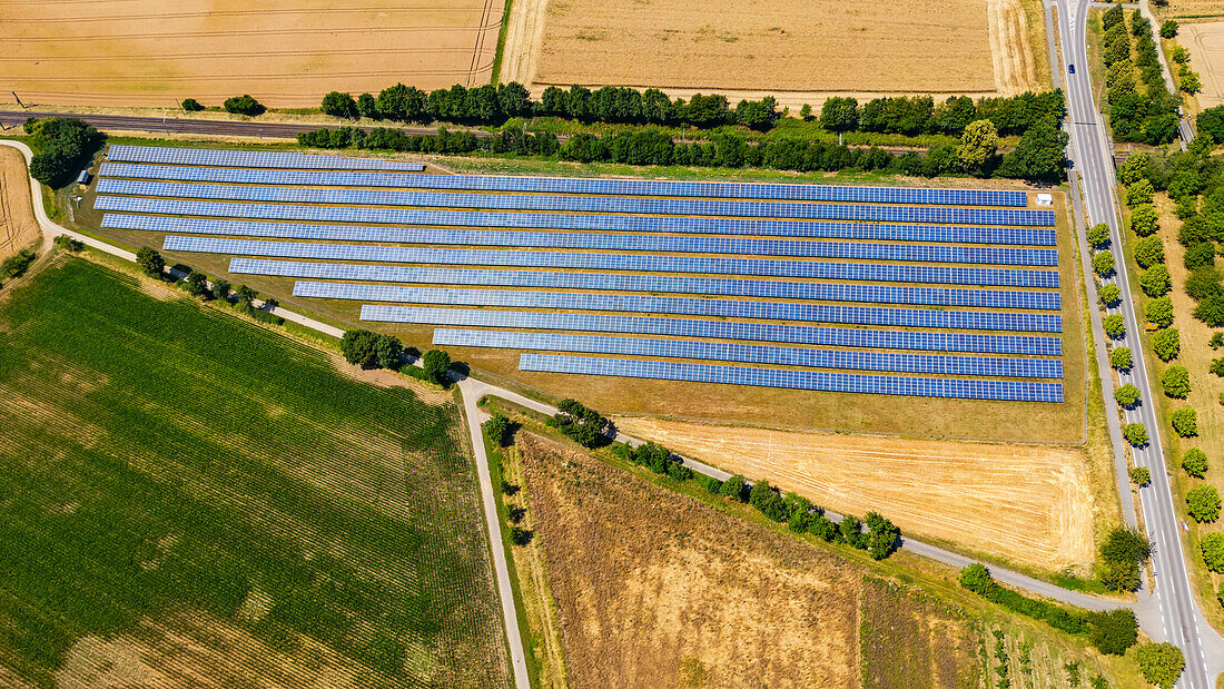 Aerial view of a ground-mounted system with photovoltaic modules next to a road and railway line, Hesse, Germany