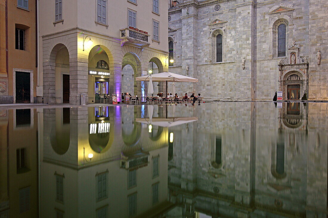 Terrace of an enoteca on the Piazza Guido Grimoldi reflected in a fountain, behind it the Cathedral di Santa Maria Assunta, Como, Lake Como, Lombardy, Italy