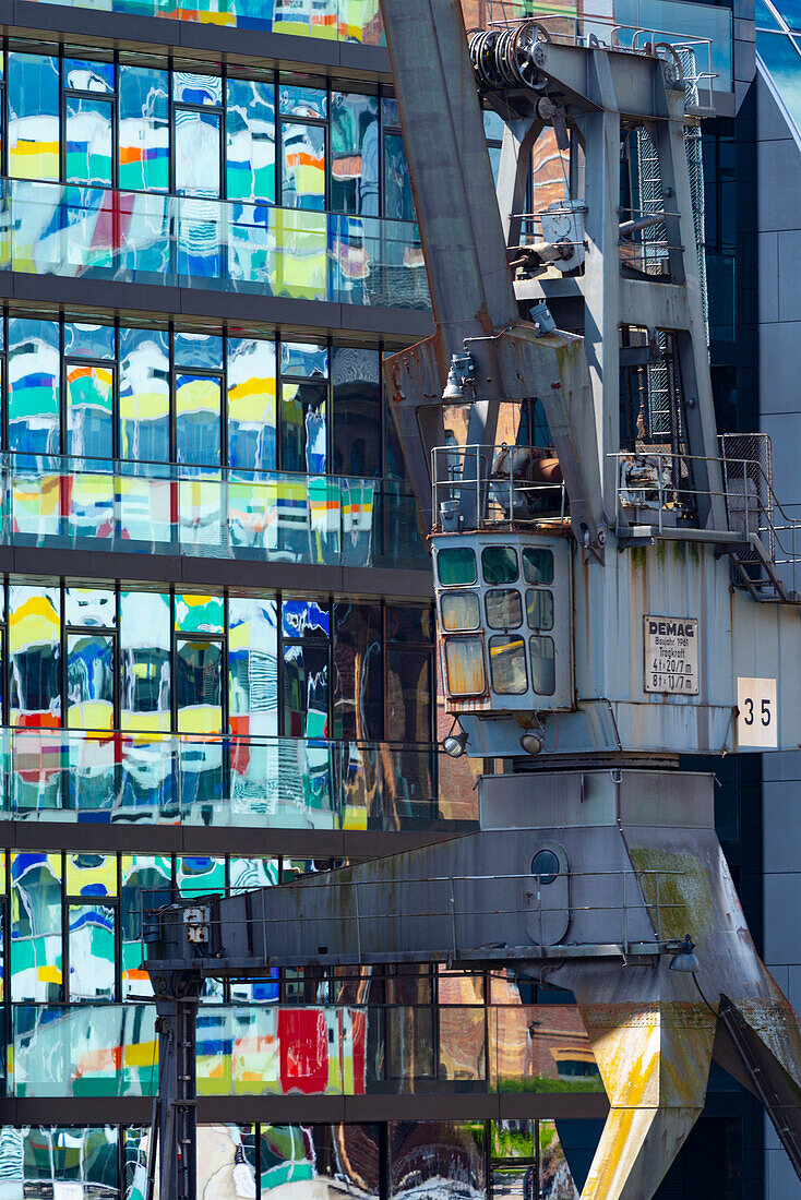 Old crane in front of the glass facade of an office building, the high-rise Colorium is reflected in it, facade with colored glass panels, architect William Alsop, Julo-Levin-Ufers in the Medienhafen, Dusseldorf, North Rhine-Westphalia, Germany, Europe