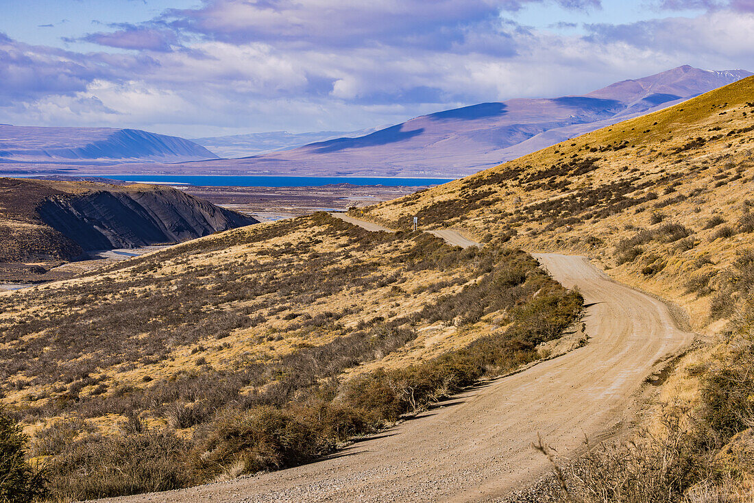 A gravel road with a distant view through the grassy landscape in Torres del Paine National Park, Chile, Patagonia, South America