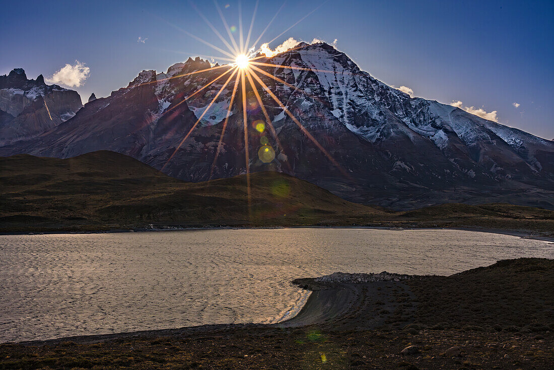 Sonnenstern über den Bergen am Torres del Paine Natiopnalpark am Lago Nordenskjöld, Chile, Patagonien, Südamerika