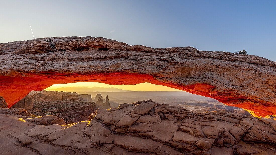 Mesa Arch in Canyonlands National Park is illuminated orange by the sun from below during sunrise.