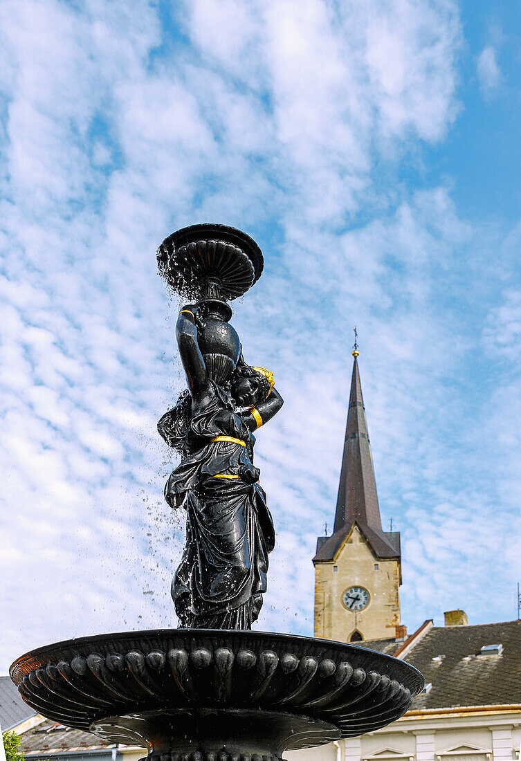 Fountain with Hygiea statue in the market square Náměstí Svobody and church tower of the Kostel svatého Tomáše z Canterbury in Mohelnice in Moravia in the Czech Republic