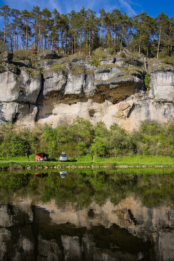 Reflection in the lake of a couple camping by car at the Bärenschlucht holiday campsite, near Pottenstein, Franconia, Bavaria, Germany