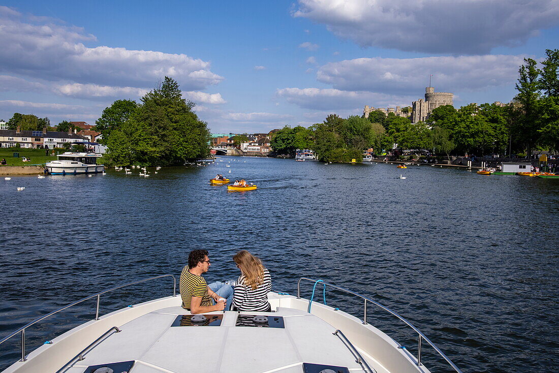 Paar am Bug von einem Le Boat Horizon 4 Hausboot auf der Themse mit Windsor Castle in der Ferne, Windsor, Berkshire, England, Vereinigtes Königreich
