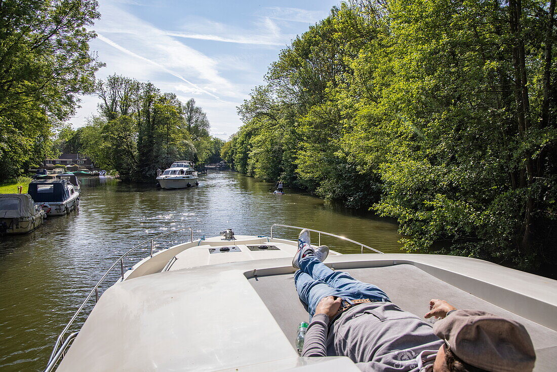Mann entspannt sich am Bug von einem Le Boat Horizon 4 Hausboot auf der Themse, Hurley, in der Nähe von Maidenhead, Berkshire, England, Vereinigtes Königreich