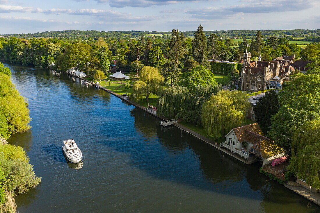 Aerial view of a Le Boat Horizon 4 houseboat passing the Oakley Court Hotel along the River Thames, Water Oakley, near Windsor, Berkshire, England, United Kingdom