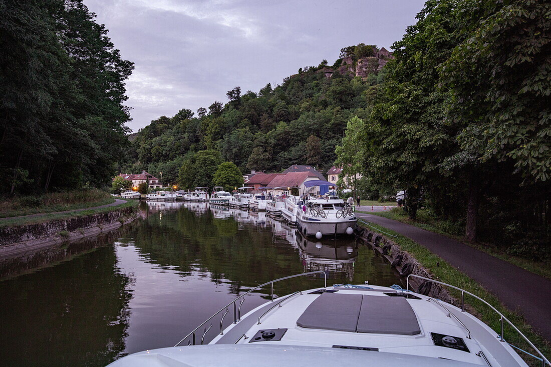 Bow of a Le Boat Horizon 5 houseboat and other houseboats on the Canal de la Marne au Rhin with Château de Lutzelbourg Castle, Lutzelbourg, Moselle, France