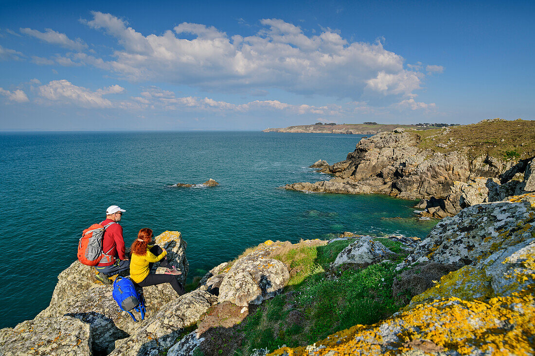 Mann und Frau beim Wandern sitzen auf Felsvorsprung und blicken auf die Küste, Cap-Sizun, GR 34, Zöllnerweg, Bretagne, Frankreich