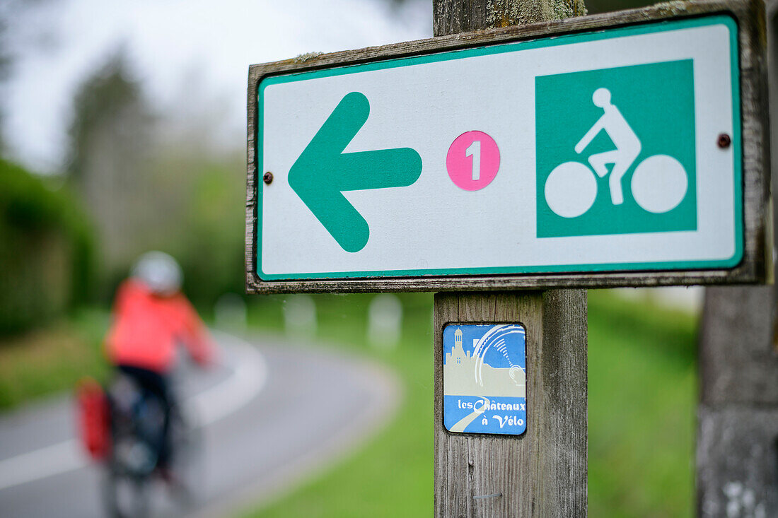 Frau beim Radfahren am Loire-Radweg mit Wegweiser im Vordergrund, Loire-Radweg, Loire-Schlösser, Loiretal, UNESCO Welterbe Loiretal, Frankreich