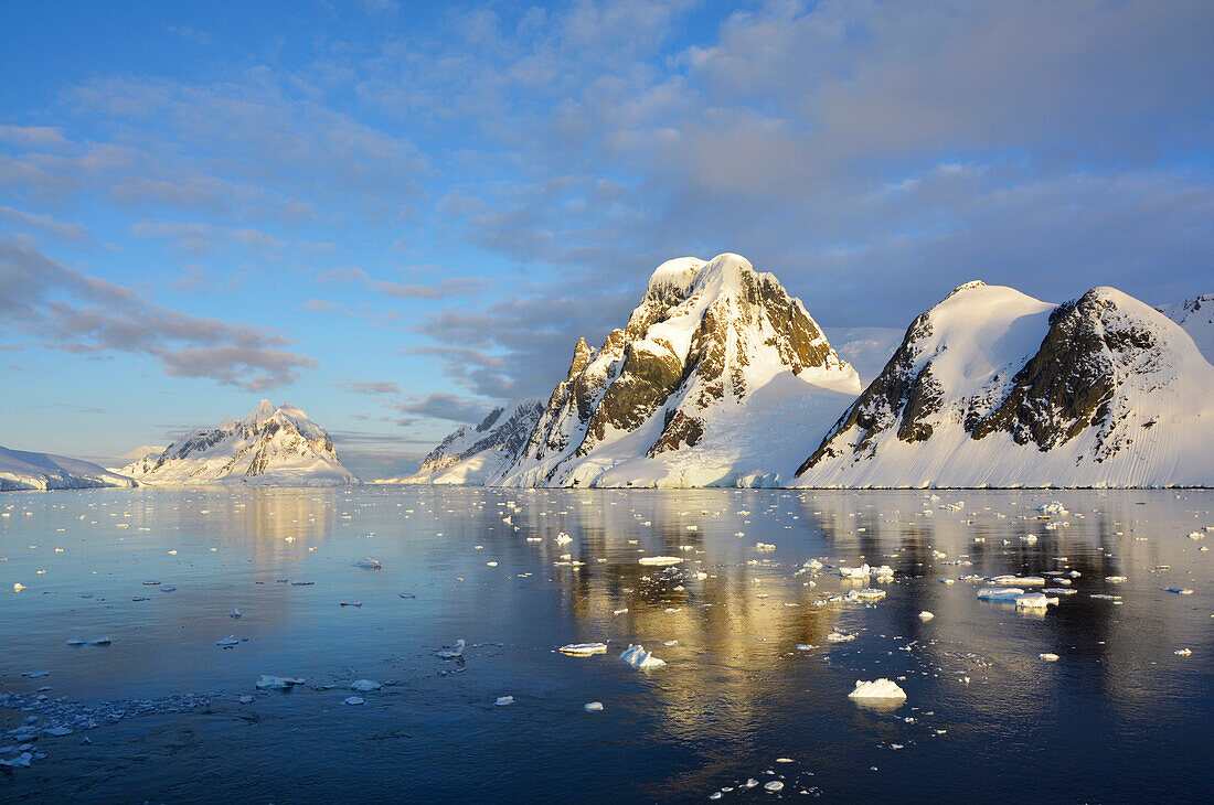 Antarktis; antarktische Halbinsel; auf der Fahrt von Petermann Island Richtung Port Charcot; Schnee bedeckte Berge; kleinere Eisschollen treiben vor der Küste; Abendstimmung; Sonne geht nicht mehr unter