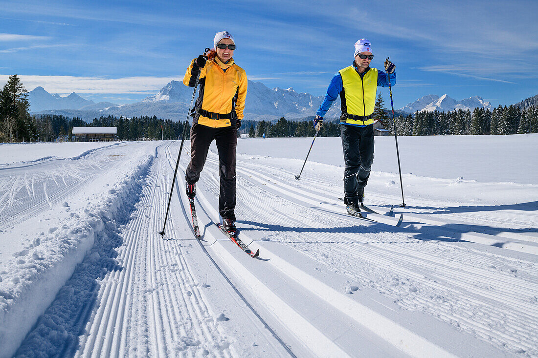 Man and woman cross-country skiing on the Krün cross-country ski trail, Sonnenloipe, Karwendel and Wetterstein in the background, Werdenfels, Upper Bavaria, Bavaria, Germany