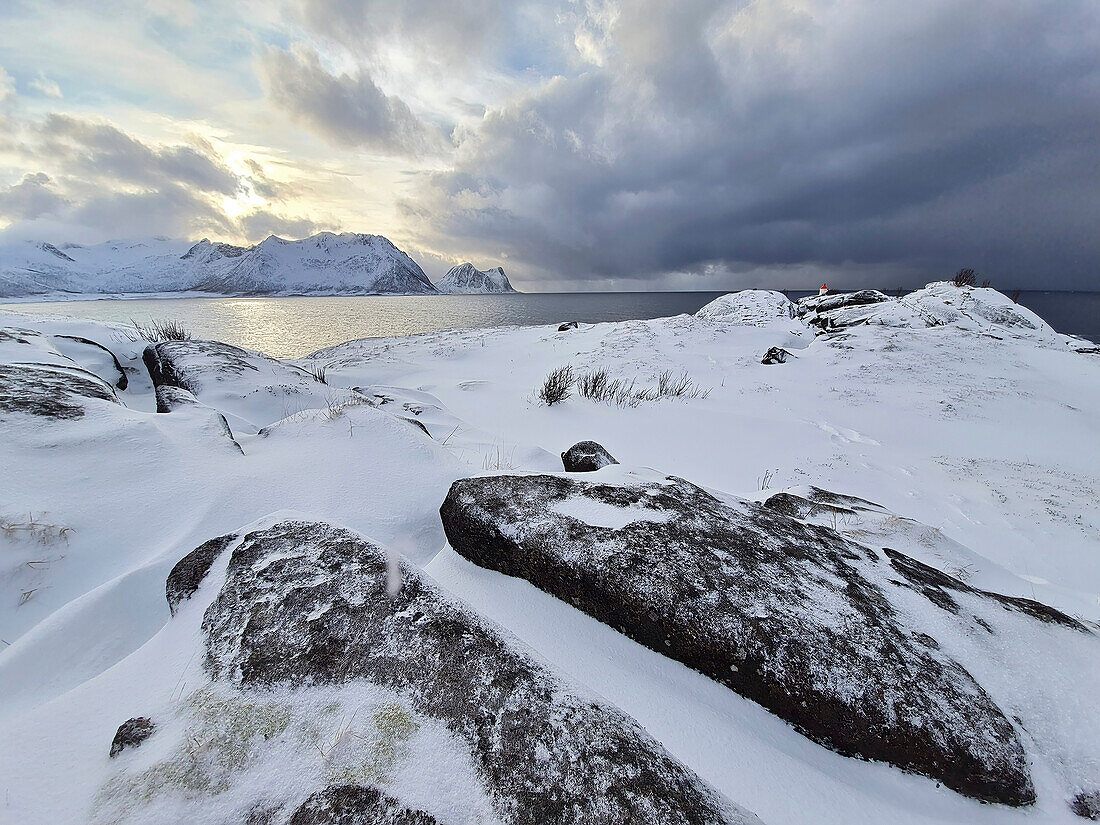 Verschneite Felsplatten auf Landzunge mit Schlechtwetterwolken, Senja, Troms og Finnmark, Norwegen