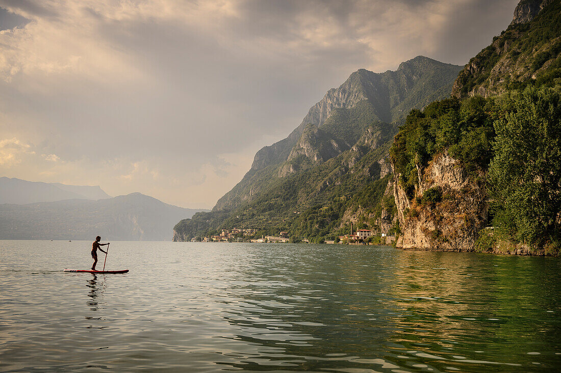 Man rides on SUP on the beach near Marone, Lake Iseo (Lago d'Iseo, also Sebino), Brescia and Bergamo, Northern Italian Lakes, Lombardy, Italy, Europe