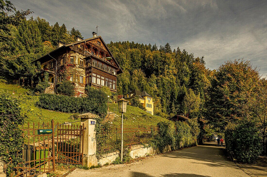 Herbstimmung mit Alpenhaus und wandernden Paar im Hintergrund an der Mondseestraße in St. Gilgen, Wolfgangsee, Bundesland Salzburg, Alpen, Österreich