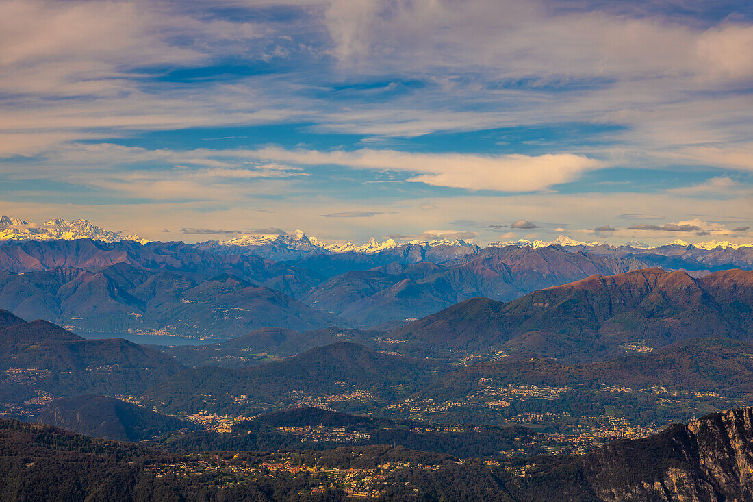 Luftaufnahme über eine wunderschöne Berglandschaft und einen schneebedeckten Berg mit schwebenden Wolken an einem sonnigen Tag in Lugano, Tessin, Schweiz.