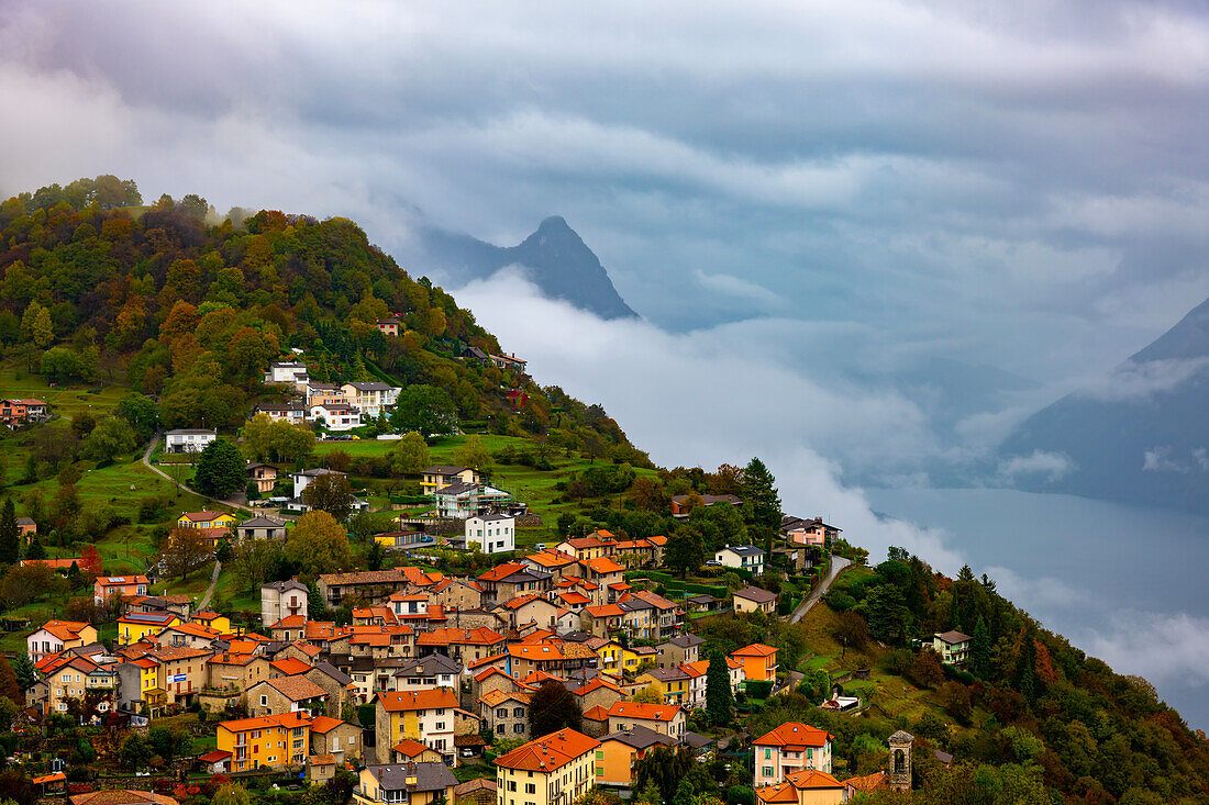 Luftaufnahme über Berglandschaft und Alpendorf Bre mit Herbstwald und Luganersee an einem bewölkten Tag in Monte Bre, Lugano, Tessin, Schweiz