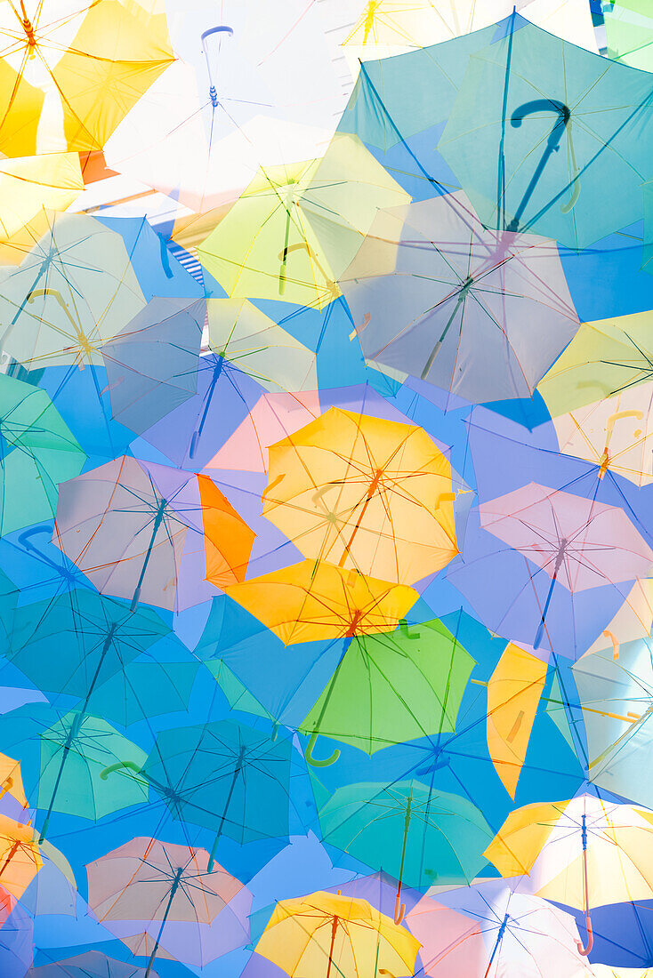 Multiple exposure of colorful umbrellas suspended over a street to provide shade in Bordeaux, France.