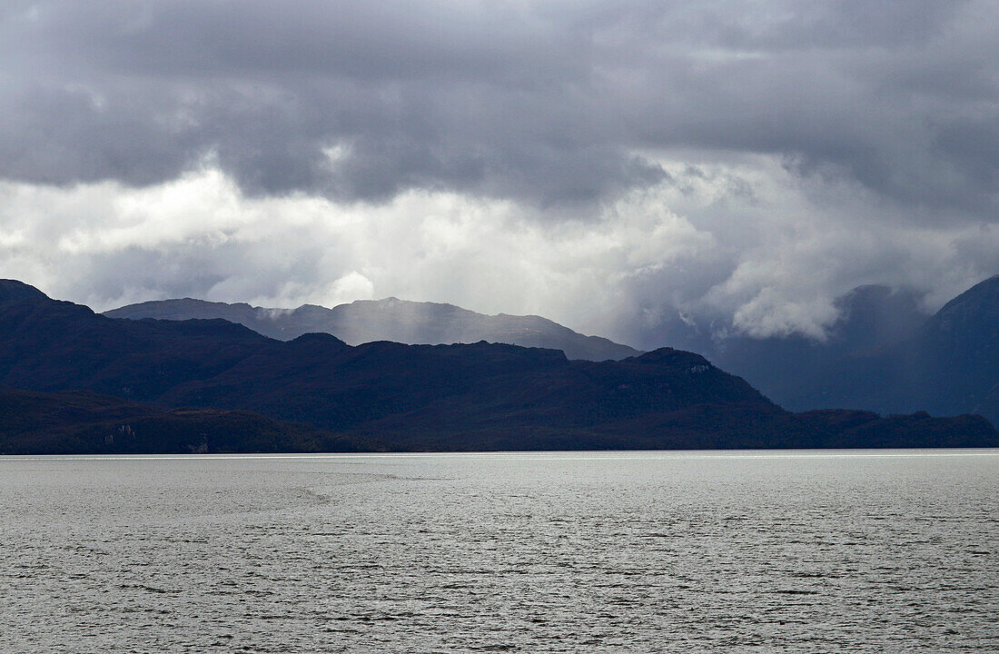 Chile; Südchile; Region Magallanes; Gebirge der südlichen Cordillera Patagonica; auf der Navimag Fähre durch die patagonischen Fjorde; Canal Messier; Sonnenstrahlen durchbrechen die Regenwolken