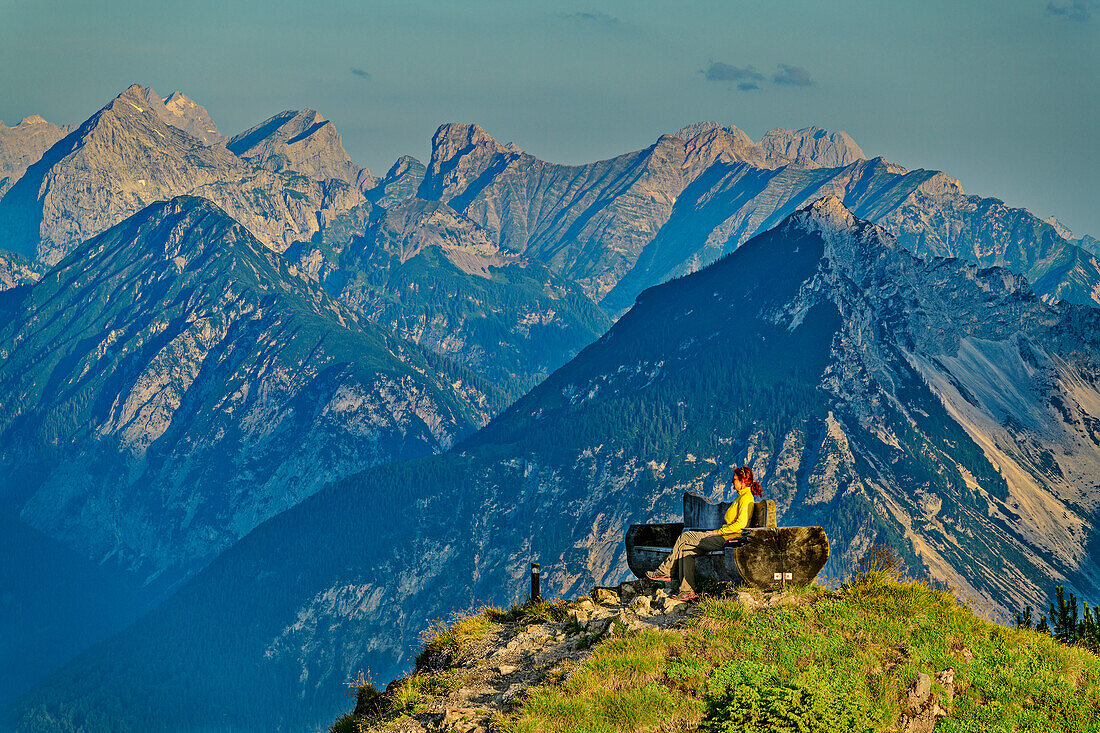 Woman hiking sits on observation bench and looks at Karwendel, from Gratlspitze, Wildschönau, Kitzbühel Alps, Tyrol, Austria