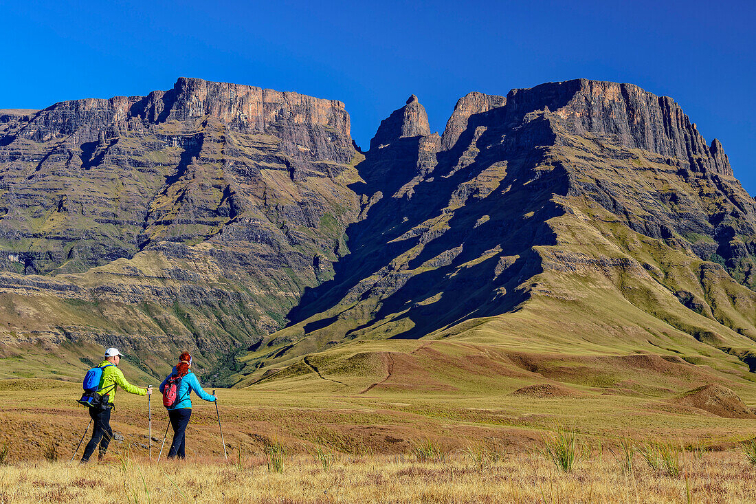 Mann und Frau beim Wandern auf Shada Ridge mit Champagne Castle im Hintergrund, Injasuthi, Drakensberge, Kwa Zulu Natal, UNESCO Welterbe Maloti-Drakensberg, Südafrika