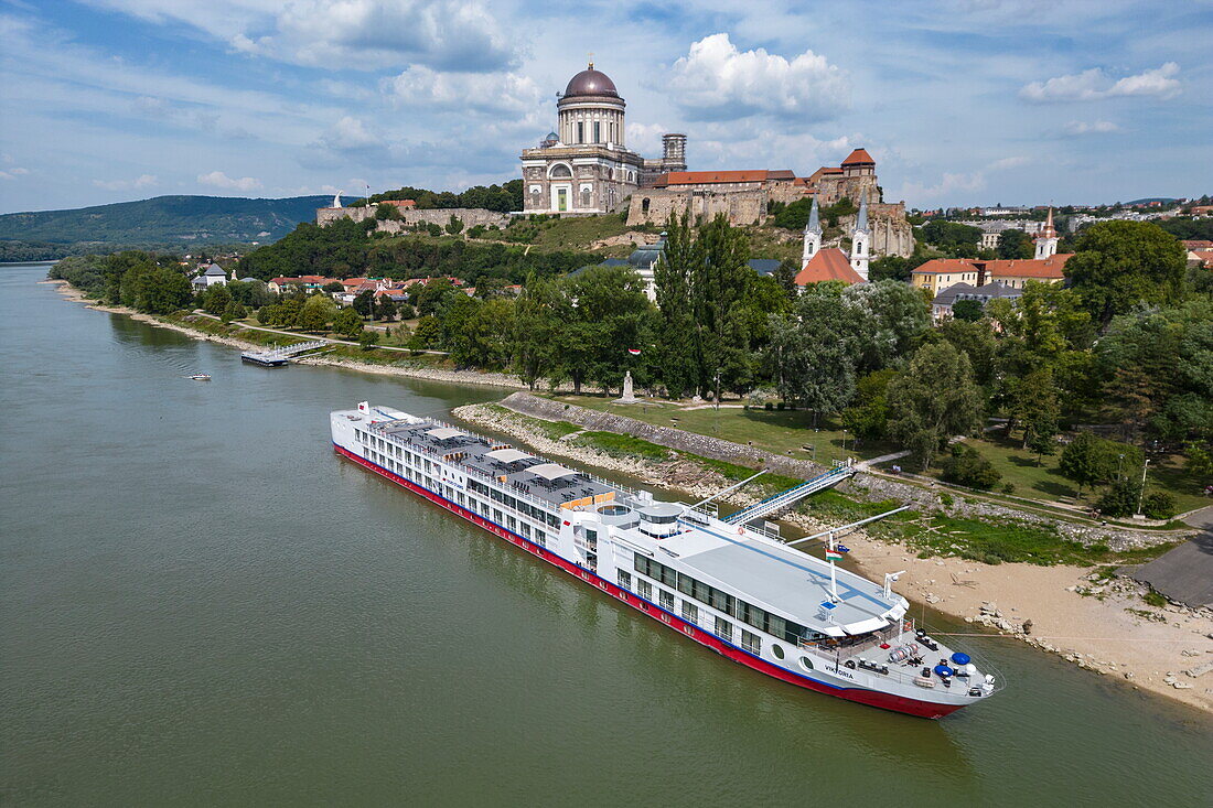 Luftaufnahme von Flusskreuzfahrtschiff Viktoria (nicko cruises), das an der Donau liegt, mit der Kathedrale von Esztergom dahinter, Esztergom, Komárom-Esztergom, Ungarn, Europa