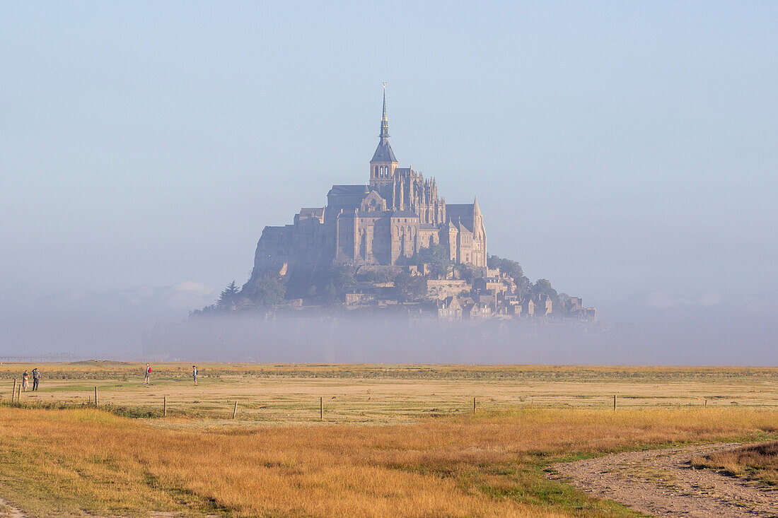 Spaziergänger auf Wiese und Nebelschwaden vor Mont Saint-Michel, Département Manche, Normandie, Frankreich