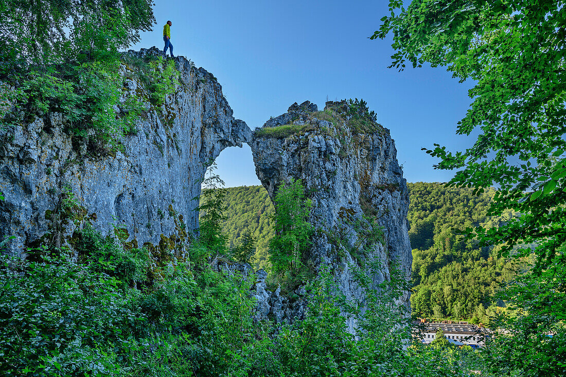 Man hiking stands on rock arch Kissing Sau, Weiler im Achtal, Blaubeuren, Swabian Alb, Baden-Württemberg, Germany