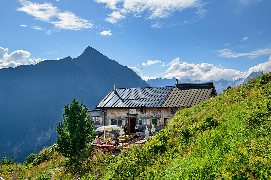 Mehrere Personen sitzen vor der Gamshütte, Dristner im Hintergrund, Gamshütte, Zillertaler Alpen, Tirol, Österreich