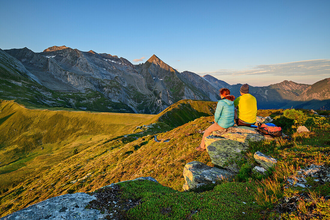 Man and woman hiking sitting on rocks and looking at Rosskopf and Höllenstein, from Tettensjoch, Tux Valley, Zillertal Alps, Tyrol, Austria