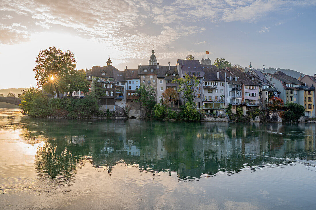 Häuserzeile am Fluss Rhein mit Laufenbrücke bei Sonnenaufgang zum Schweizer Stadtteil Laufenburg (AG), Aargau, Schweiz