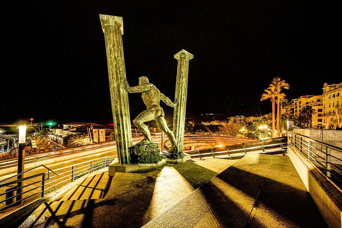 Statue der Säulen des Herkules an der Seepromenade von Ceuta bei Nacht im Hintergrund der Hafen, Ceuta, Straße von Gibraltar, Spanien