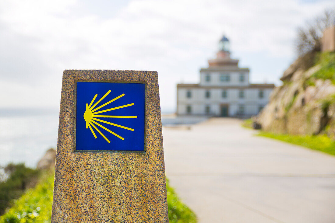  The scallop shell at the end of the Way of St. James in the background the lighthouse at Cape Finisterre, Galicia, Spain 