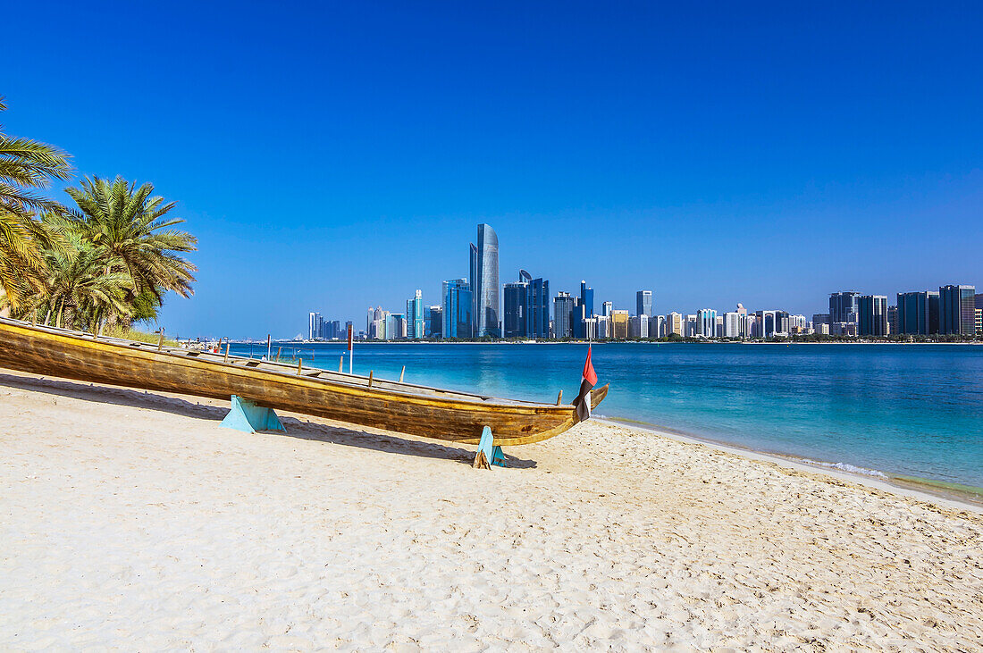 Holzkanu am Sandstrand vor moderner Skyline, in Abu Dhabi, Vereinigte Arabische Emirate, Arabische Halbinsel, Persischer Golf