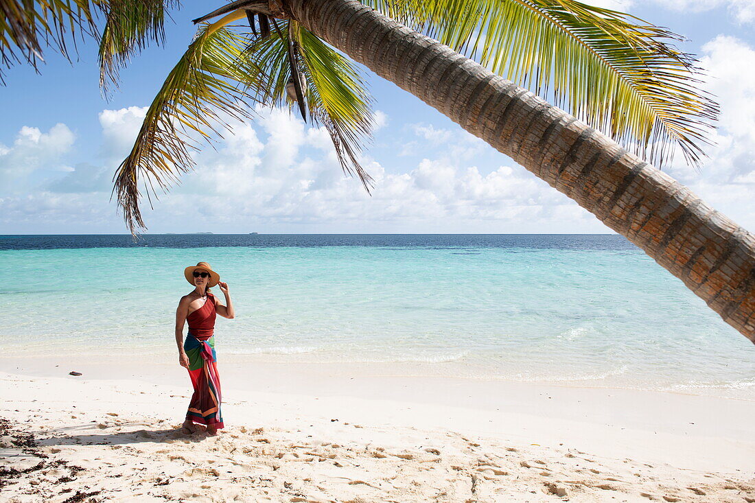 Kokospalme und Frau in buntem Kleid die am Traumstrand der Insel Bijoutier entlang spaziert, Bijoutier Island, Alphonse Group, Äußere Seychellen, Seychellen, Indischer Ozean