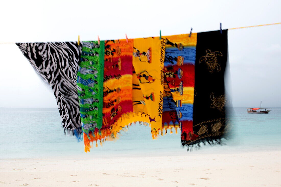  Colorful fabric towels blow in the wind and dry on clothesline on the beach, near Stonetown, Zanzibar City, Zanzibar, Tanzania, Africa 