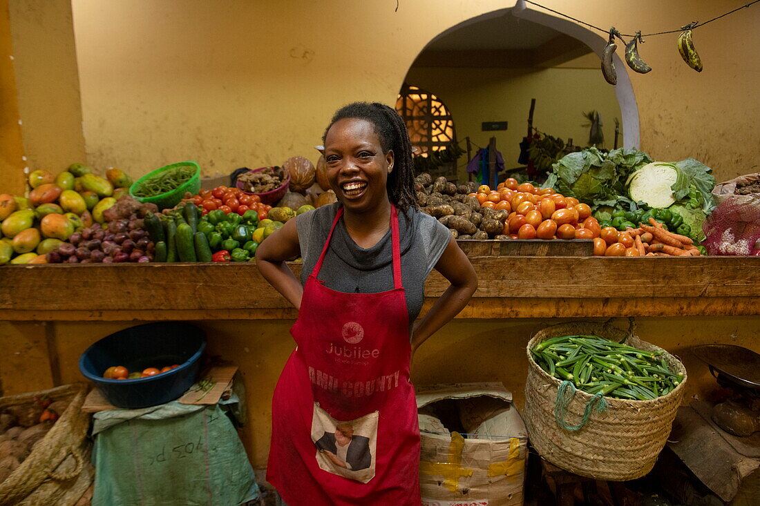 Einheimische fröhliche Frau an einem Obst- und Gemüsestand in der Markthalle, Lamu, Insel Lamu, Kenia, Afrika
