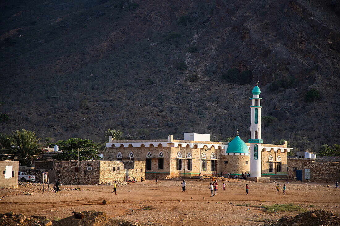  Boys play football on a dirt pitch with a mosque behind, Socotra Island, Yemen, Middle East 