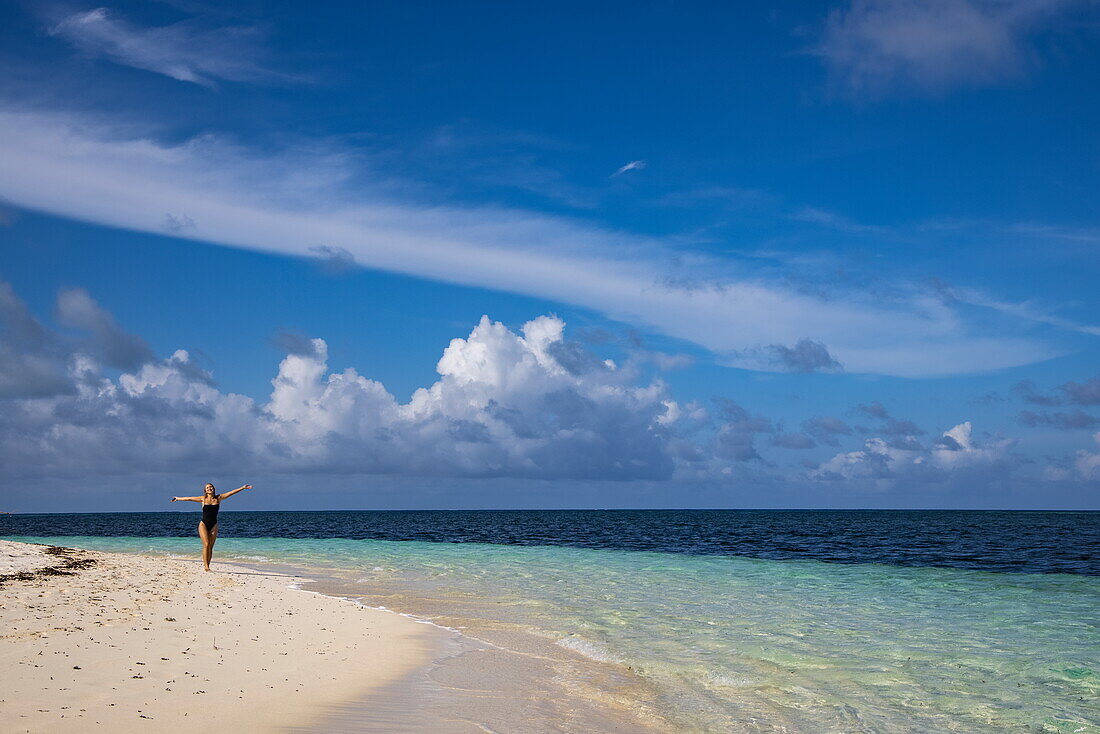  Woman spreads her arms while strolling along beach of Bijoutier Island, Bijoutier Island, Alphonse Group, Outer Seychelles, Seychelles, Indian Ocean 