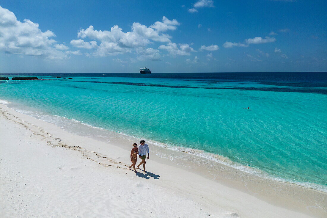 Aerial view of a couple walking along the beach with the expedition cruise ship SH Diana (Swan Hellenic) in the distance, Assumption Island, Outer Islands, Seychelles, Indian Ocean 