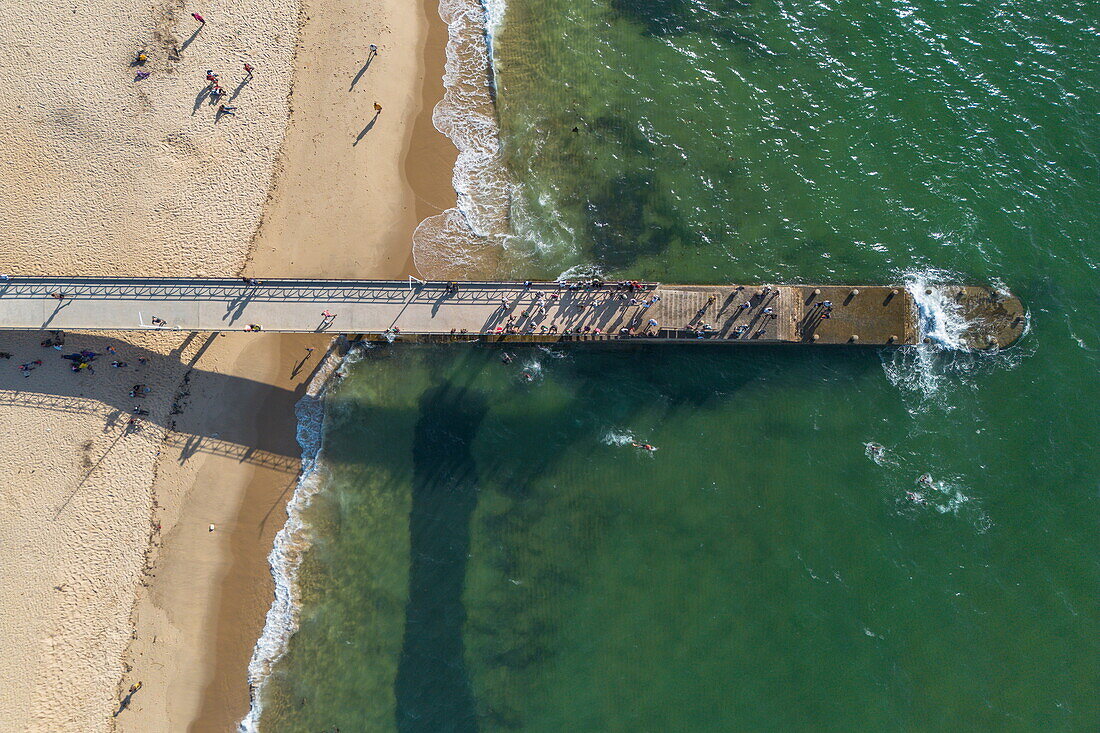 Luftaufnahme eines langen Piers am Strand mit Menschen, die ins Wasser springen, Mahajanga, Boeny, Madagaskar, Indischer Ozean