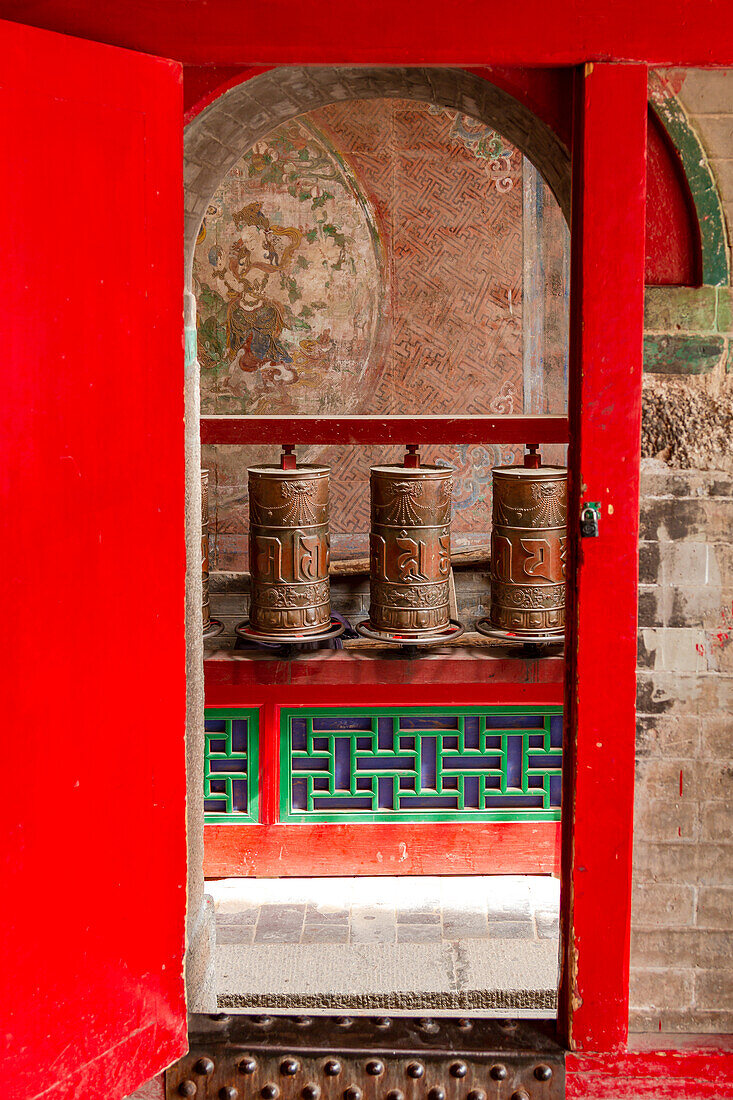 Gebetsmühlen hinter einem Tor in einem tibetischen Tempel der Klosteranlage Kumbum Jampaling im chinesischen Xining, Asien